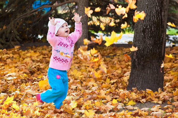 Девочка подбрасывает осенние листья в парке