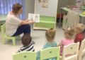 Воспитательница показывает детям, сидящим на стульях, картинку в книжке