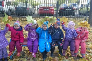 Дети с осенними листьями в руках сидят на лавочке