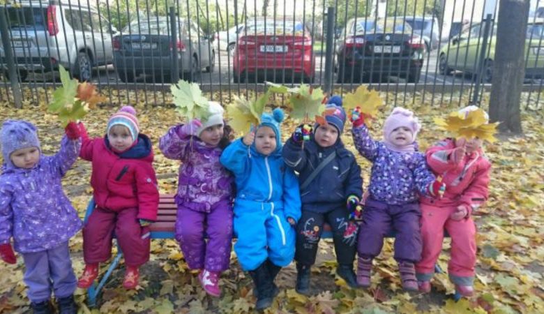 Дети с осенними листьями в руках сидят на лавочке