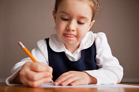Девочка пишет в тетради карандашом, от сосредоточенности высунула язык