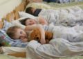 Девочка с мишкой лежит в кровати в детском саду