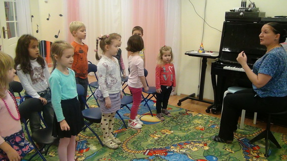 Педагог сидит за фортепиано, дети перед ним поют