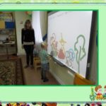 Мальчик рисует на интерактивной доске, воспитатель стоит рядом