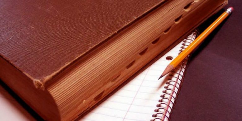 Книга в коричневом переплёте лежит на блокноте, рядом простой карандаш