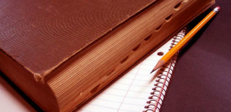 Книга в коричневом переплёте лежит на блокноте, рядом простой карандаш