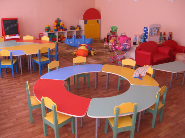 Круглый стол из четырёх сегментов, стулья, на заднем плане два красных кресла