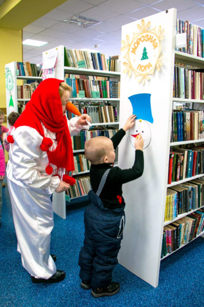 Ребёнок выполняет квест в библиотеке, педагог в костюме снеговика стоит рядом