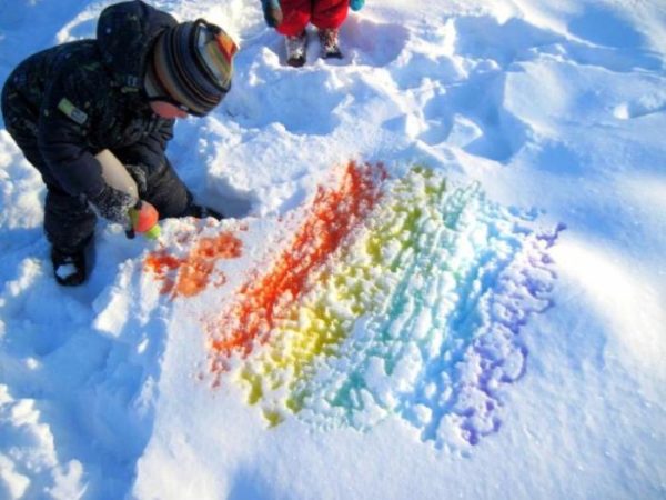 Мальчик раскрашивает снег в цвета радуги