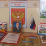 Плакат с российским гербом, фото Путина, книжки и папки на столе