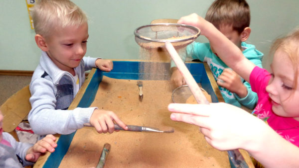 Дети просеивают песок через сито и работают с кисточками