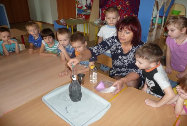 Дети и воспитатель наблюдают за самостоятельно изготовленным макетом вулкана
