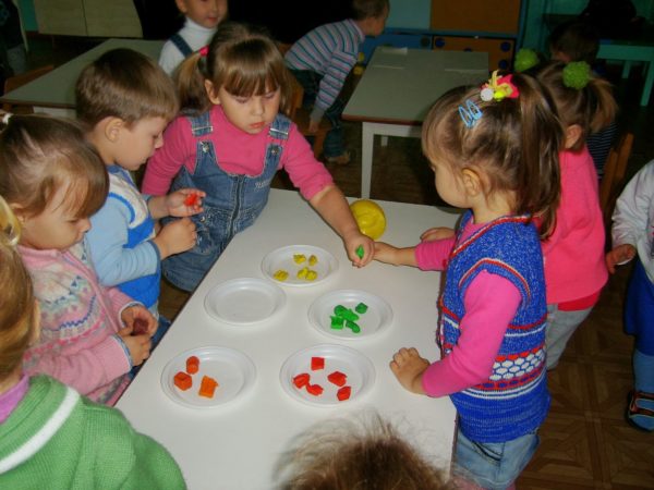 Дети стоят возле стола, на котором разложены кусочки разноцветного пластилина