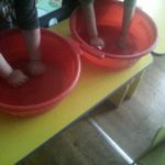Два ребёнка делают пальчиковую гимнастику в красных тазах с водой
