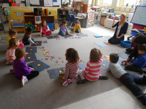Дети и воспитательница сидят по кругу на полу, собирают картинку из фигур