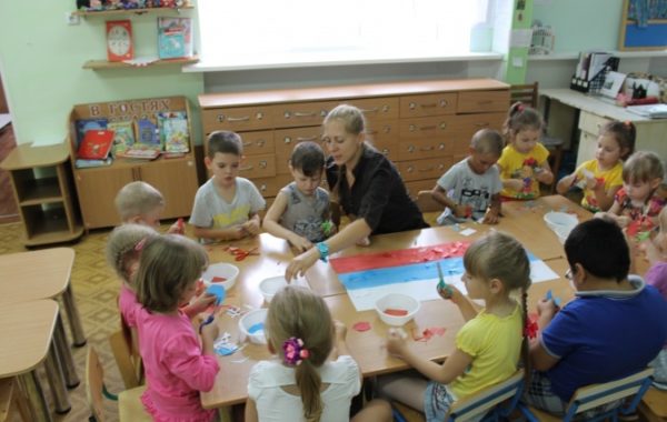 Дети за столом делают аппликацию российского флага