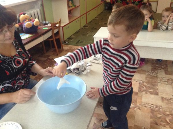 Мальчик опускает мокрую салфетку в таз с водой