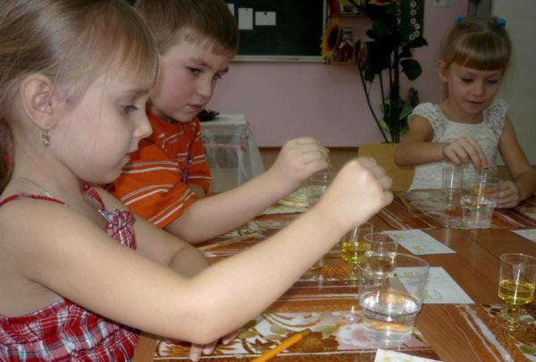 Трое детей, сидя за столом, проводят эксперимент с водой и маслом