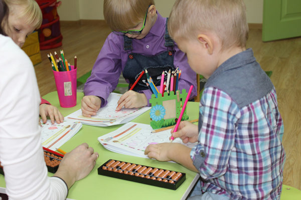Дети за небольшим столом рисуют карандашами линии на листочках