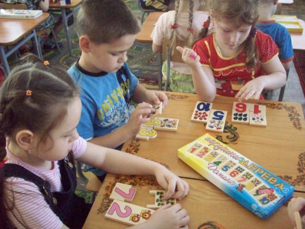 Две девочки и мальчик соотносят таблички с цифрами с требуемым количеством предметов