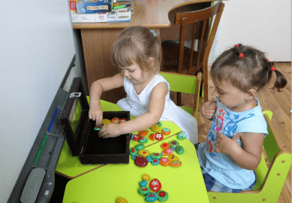 Две девочки играют с окрашенными камешками