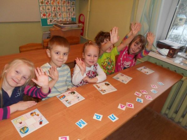 Пятеро детей за столом подбирают буквы к изображённым на карточках предметам