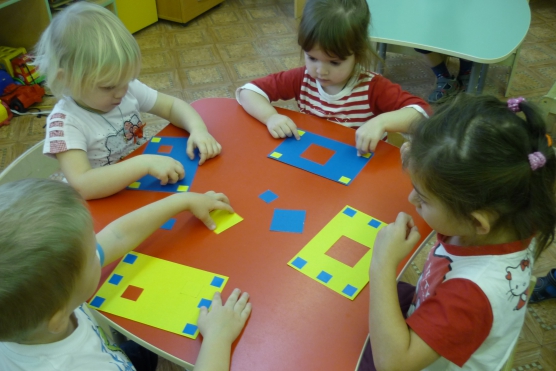 Четверо детей вкладывают разного размера квадраты в подходящие отверстия на листах, лежащих перед ними