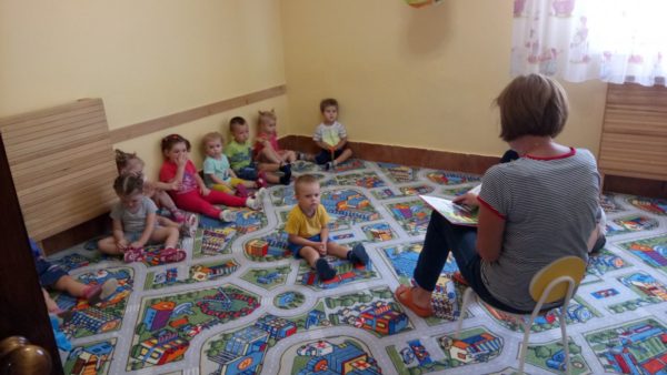 Воспитательница читает книгу детям, сидящим на ковре