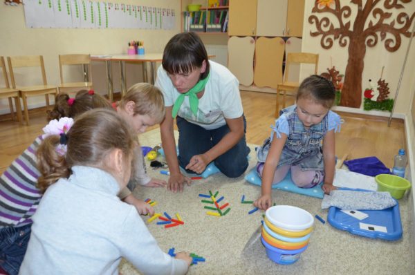 Дети и педагог играют со счётными палочками на ковре