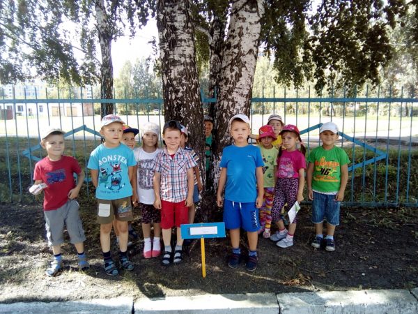 Дети стоят под деревом рядом с табличкой