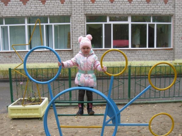 Девочка на турнике перед зданием детского сада