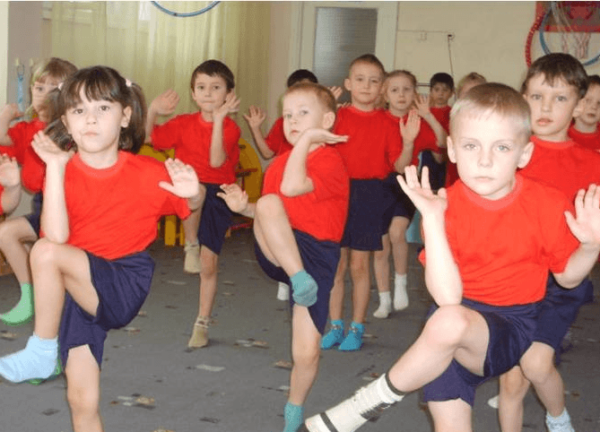 Дети в спортивной форме делают упражнение, поднимая колено к локтю