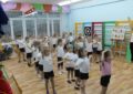 Дети в спортивной форме выполняют упражнение с поднятыми вверх руками