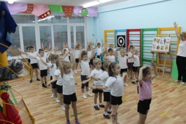 Дети в спортивной форме выполняют упражнение с поднятыми вверх руками