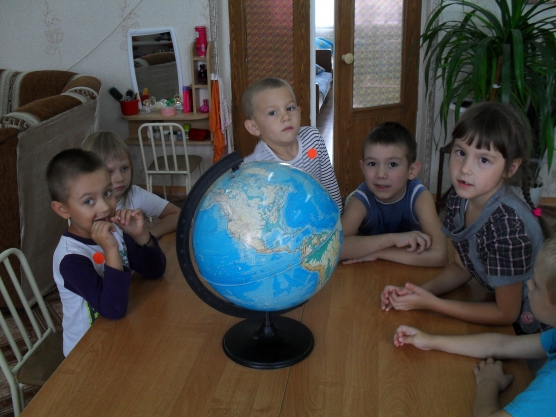 Дети сидят за столом вокруг глобуса
