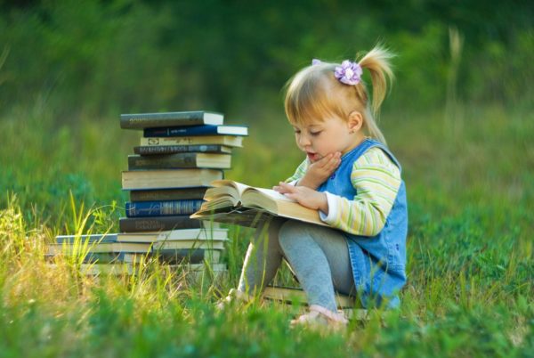 Стопка книг и девочка на полянке читает