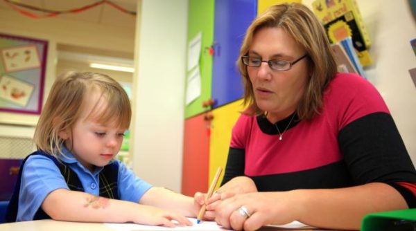 Воспитатель помогает девочке писать ручкой