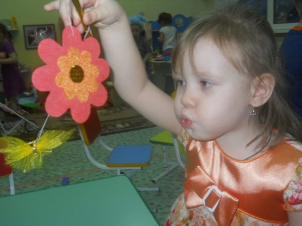 Девочка дует на бумажный цветок и бабочку