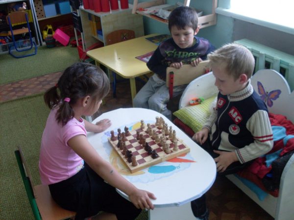 Мальчик и девочка играют в шахматы, а другой мальчик наблюдает