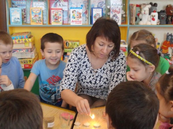 Воспитатель проводит для детей опыт со свечой