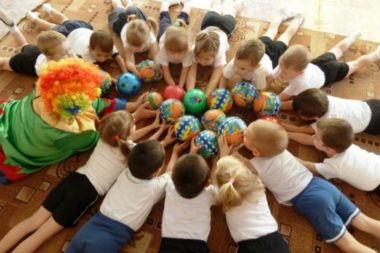 Дети и педагог в костюме клоуна с мячиками лежат на полу