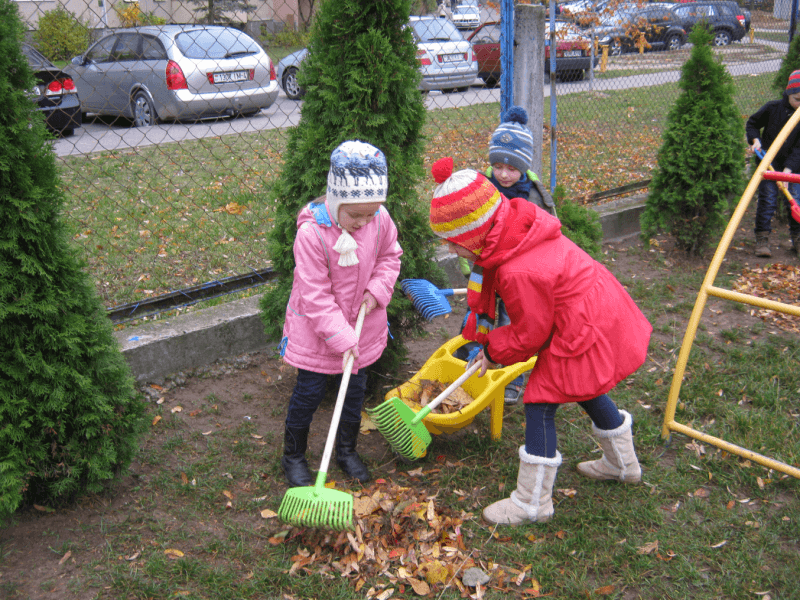Дети сгребают осенние листья на участке