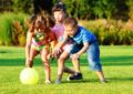 Две девочки и мальчик играют на лужайке в мяч