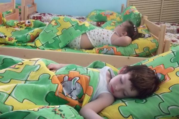 Ребёнок спит в кроватке под одеялом в зелёном пододеяльнике