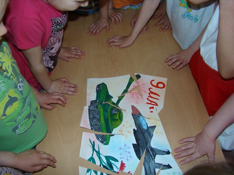 Дети стоят над пазлом-рисунком танка и самолёта