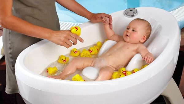 Младенец купается в ванночке с игрушечными уточками