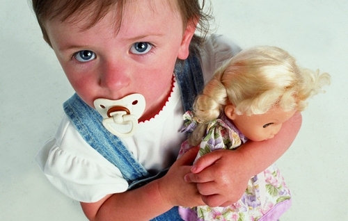 Девочка с пустышкой во рту крепко прижимает к себе куклу