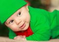Малыш в зелёном костюме и шапочке лежит на животе