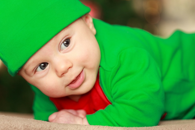 Малыш в зелёном костюме и шапочке лежит на животе